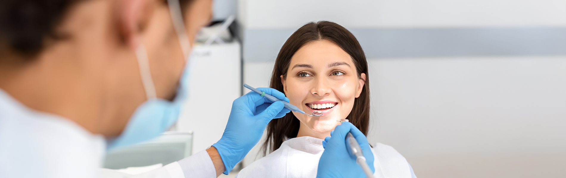 A person is seated in a dental chair, receiving care from a dental professional who stands behind them.