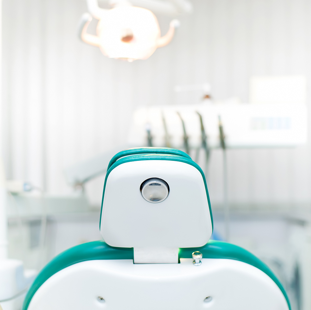 The image shows a dental chair in a dental office setting, with a green lamp and other dental equipment visible.