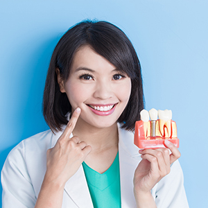 A woman in a white lab coat is holding up a red toothbrush and pointing at it with her finger, smiling at the camera.