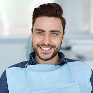 A man with a beard is sitting in a dental chair, smiling at the camera.