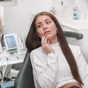 The image shows a woman sitting in a dental chair, looking at her hand with a contemplative expression, while a dentist attends to her.